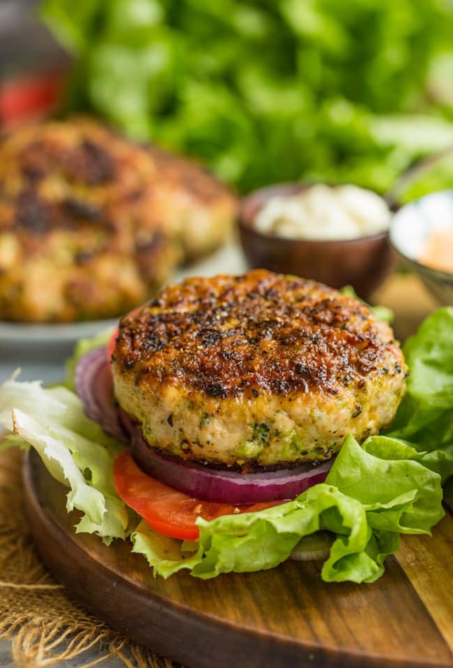 Broccoli Cheddar Chicken Burger on a lettuce leaf with onion & tomato