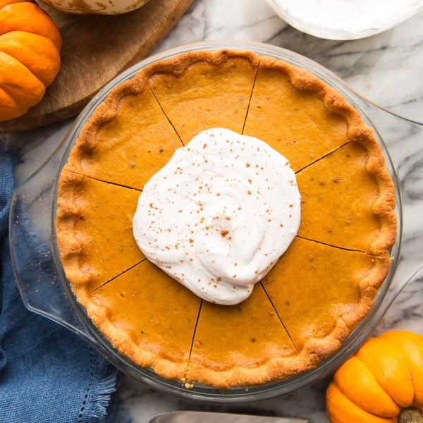 paleo pumpkin pie topped with coconut whipped cream surrounded by pumpkins