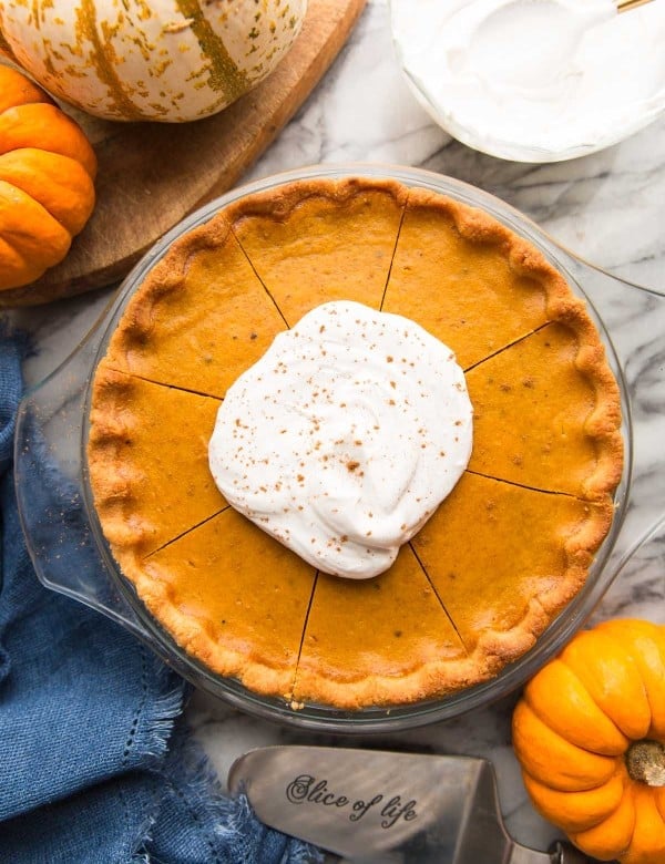 paleo pumpkin pie topped with coconut whipped cream surrounded by pumpkins