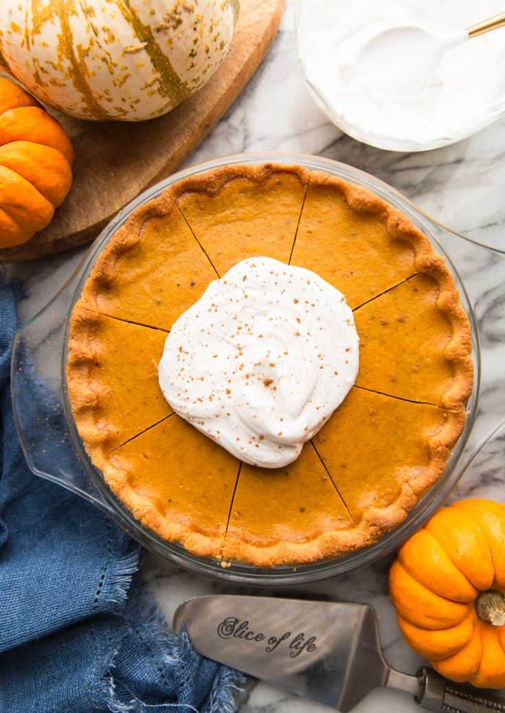 paleo pumpkin pie topped with coconut whipped cream surrounded by pumpkins