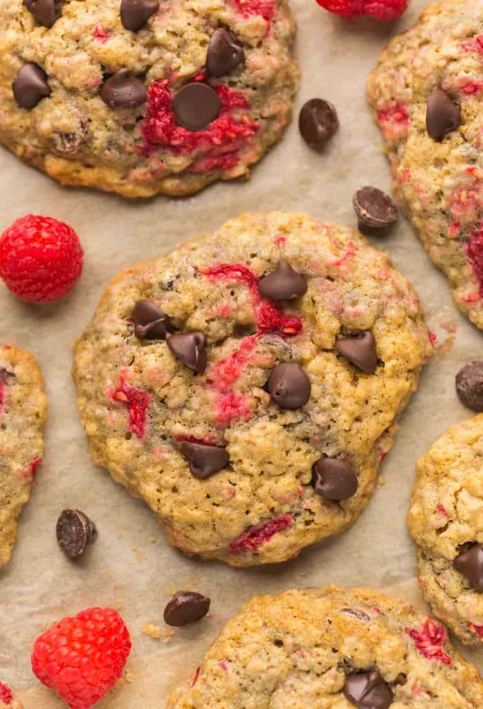 Oatmeal Raspberry Chocolate Chip Cookies on baking paper surrounded by raspberries and chocolate chips