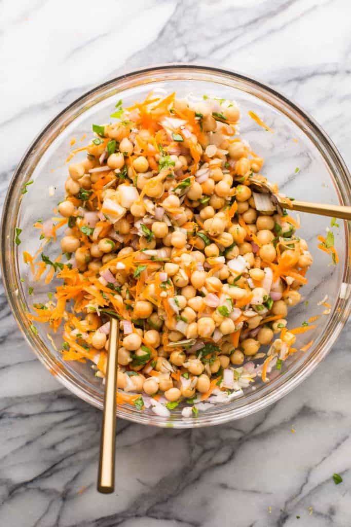 a mixing bowl full of Sweet Shallot Chickpea Salad ingredients: carrot, chickpea, salad and herbs