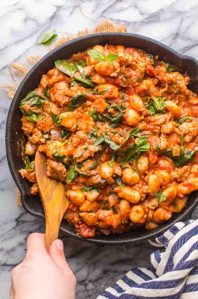 Fennel & Spinach Sausage Gnocchi in a cast iron skillet with wooden spoon stirring the pot 