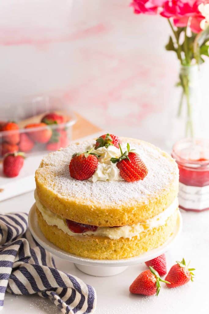 Gluten Free Victoria Sponge Cake on a cake platter topped with strawberries & whipped cream