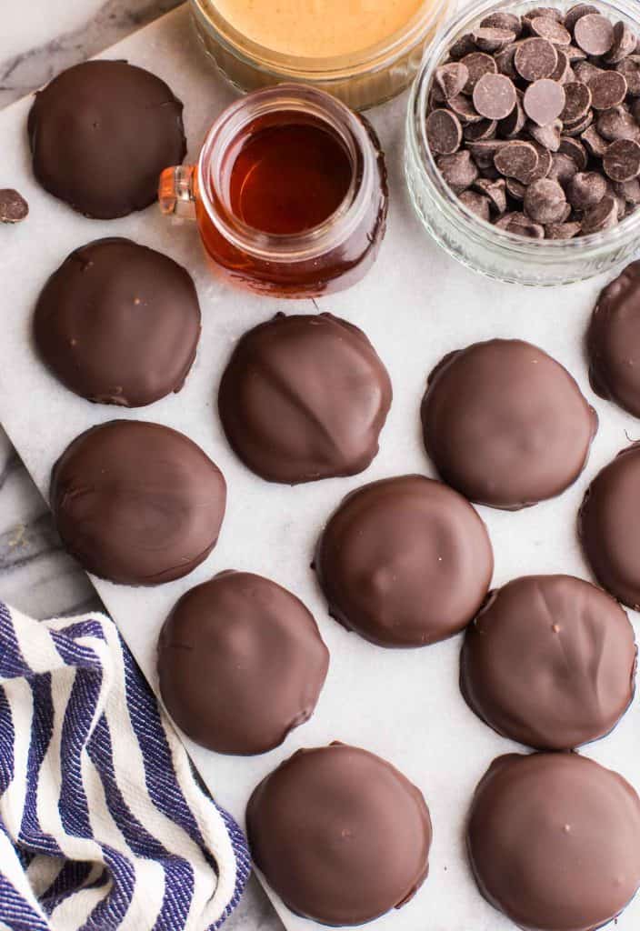 tagalongs sitting on a cutting board surrounded by chocolate chips and maple syrup