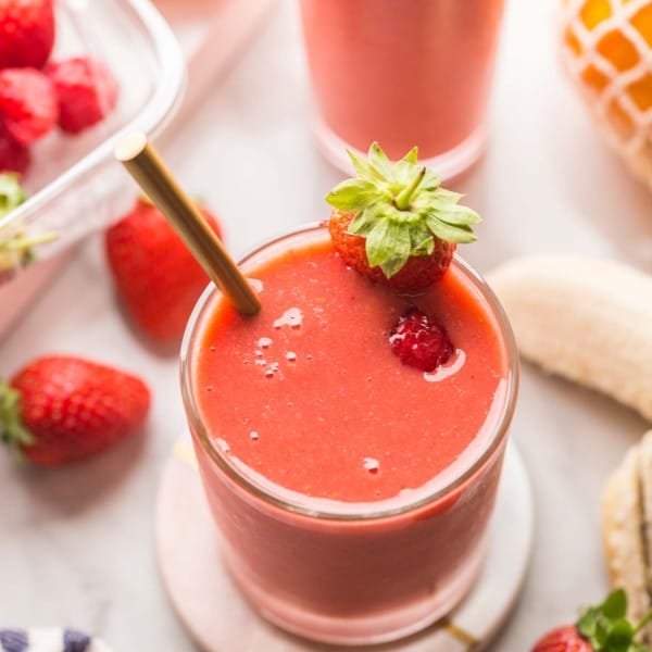 berry ginger smoothie on a coaster surrounded by fruit