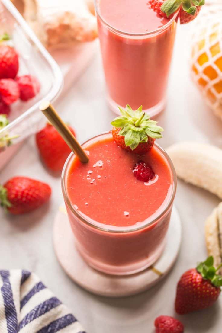 berry ginger smoothie on a coaster surrounded by fruit