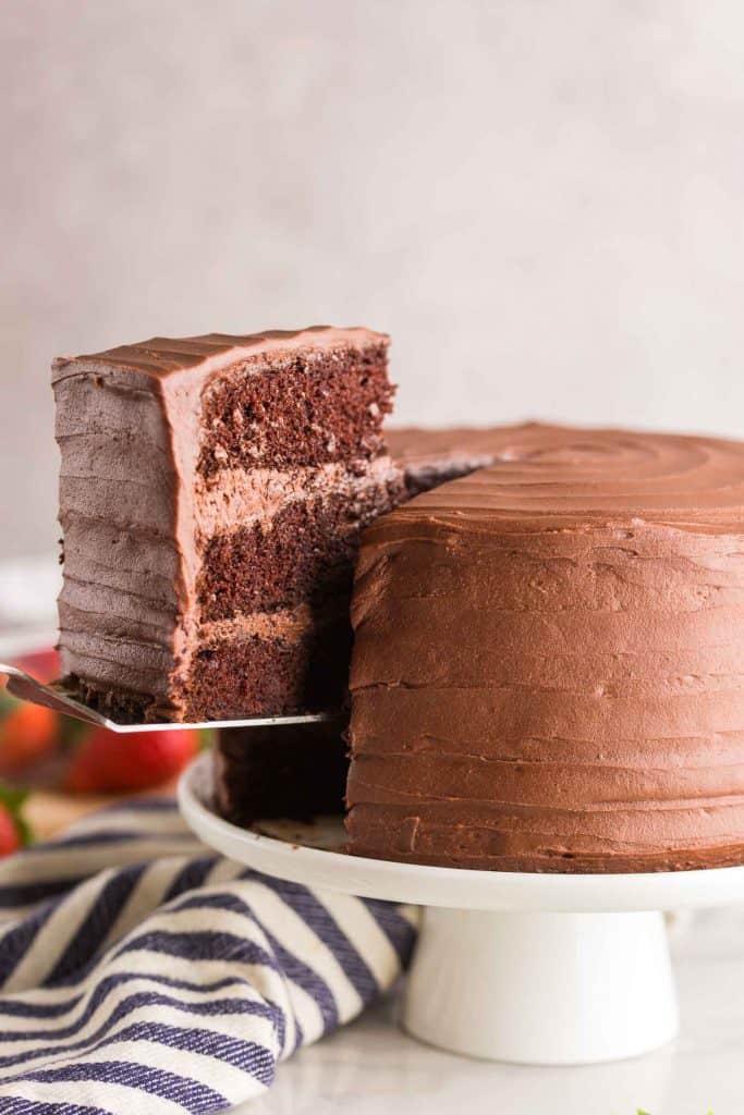 gluten free chocolate cake with a slice being picked up on a white cake stand