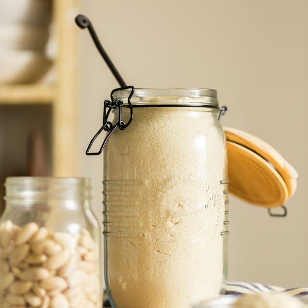 a jar of almond flour with a spoon stick out with a jar or whole almonds next to it