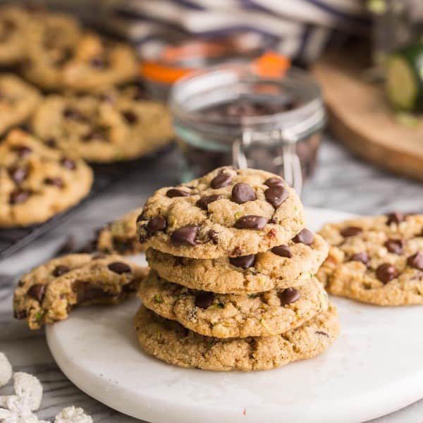 a small stack of almond flour zucchini cookies on a round serving board with chocolate chips sprinkled around