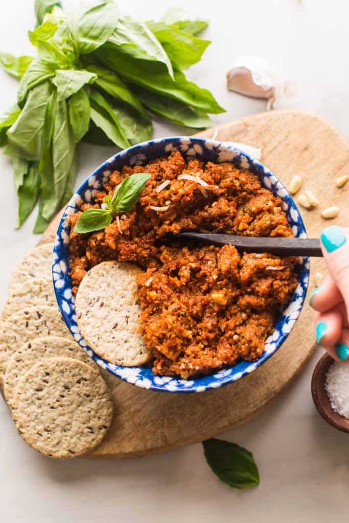 pesto rosso in a bowl topped with basil and a cracker 