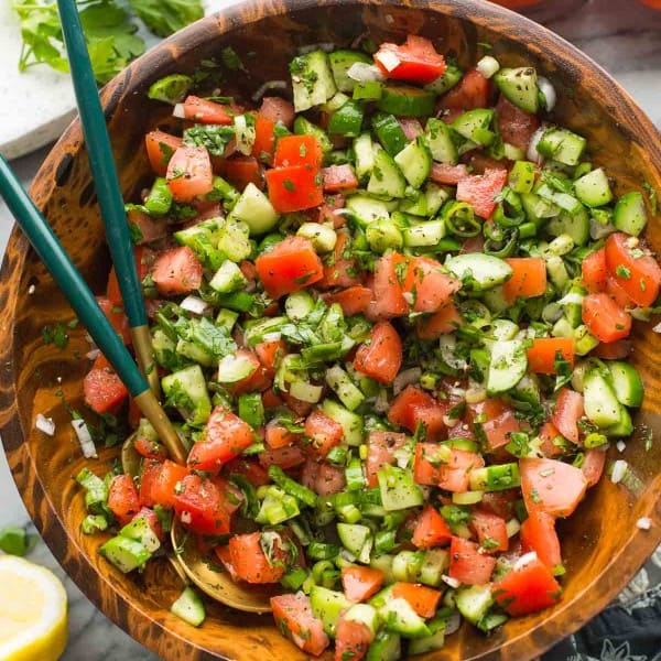 shirazi salad in a wooden salad bowl with a couple of salad tongs