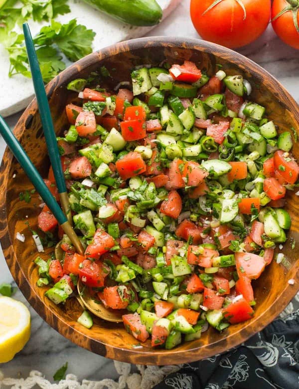 shirazi salad in a wooden salad bowl with a couple of salad tongs