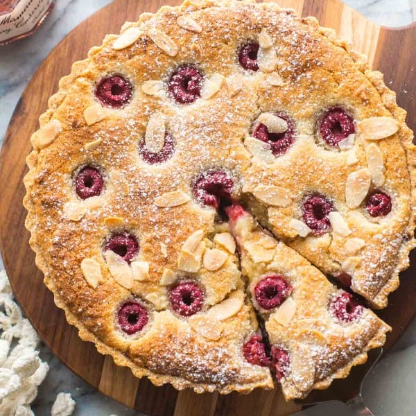 vegan bakewell tart on a wooden serving board with a slice cut out