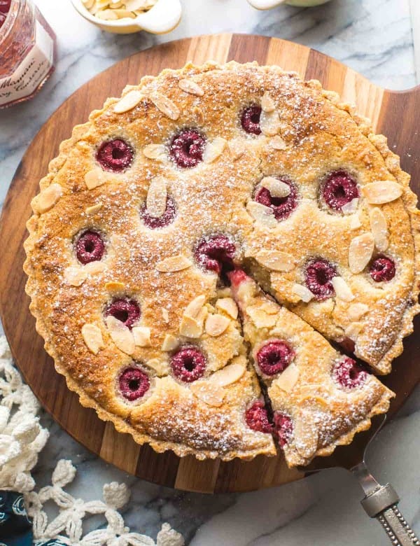 vegan bakewell tart on a wooden serving board with a slice cut out