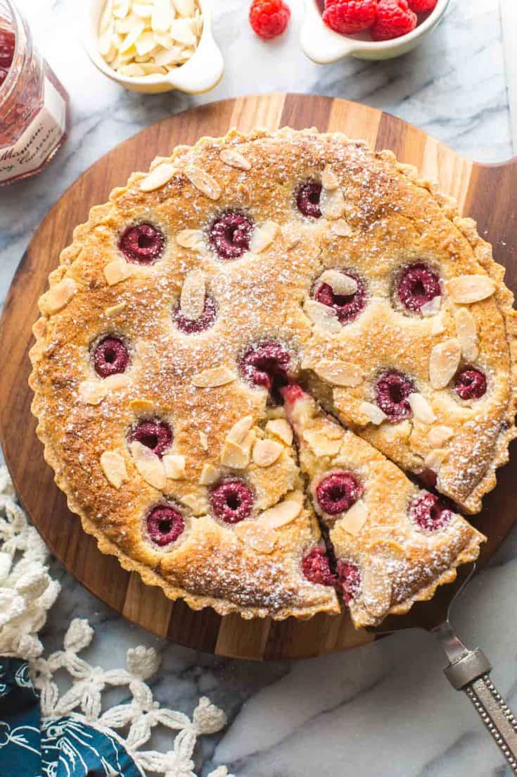 vegan bakewell tart on a wooden serving board with a slice cut out