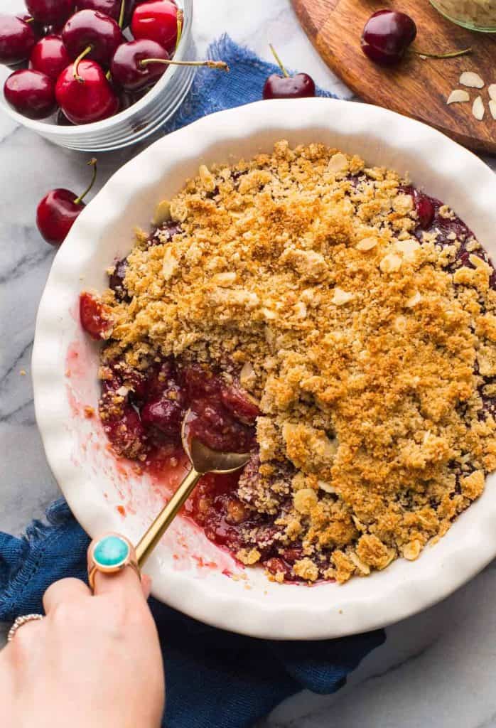 Grain Free Cherry Crumble in a pie dish surrounded by cherries