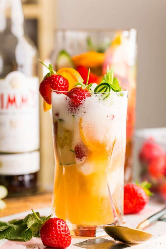 a pimm's cup float topped with fresh strawberries and cucumber 