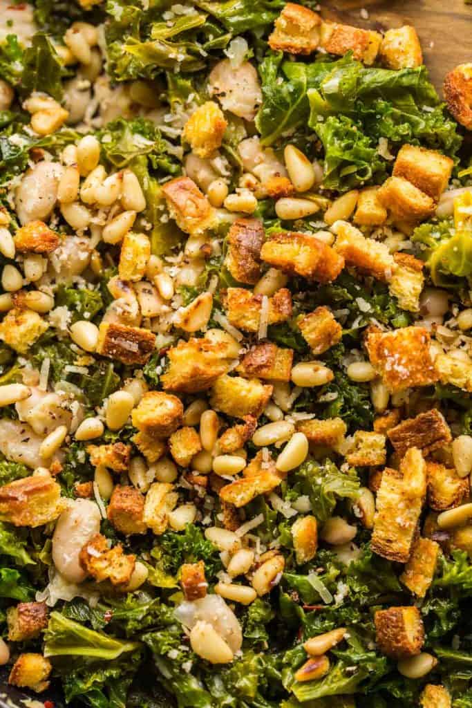 up close picture of cannelini and kale stir fry in a skillet topped with toasted bread and pine nuts