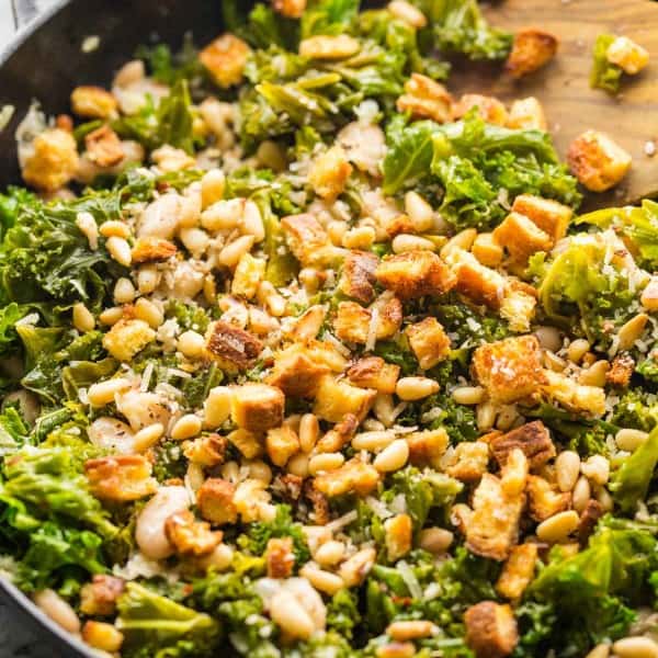kale and creamy cannelini skillet topped with toasted bread and pine nuts in a cast iron pan