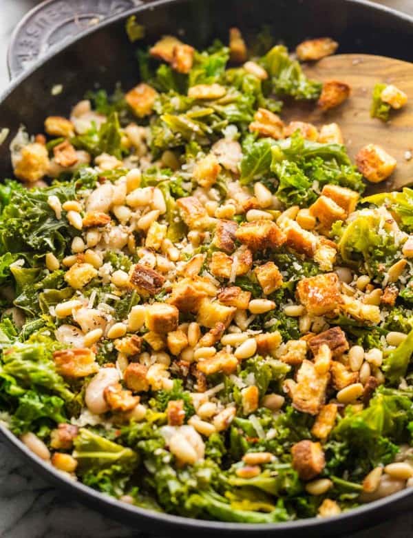 kale and creamy cannelini skillet topped with toasted bread and pine nuts in a cast iron pan