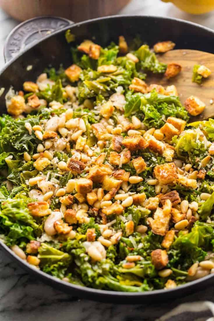 kale and creamy cannelini skillet topped with toasted bread and pine nuts in a cast iron pan