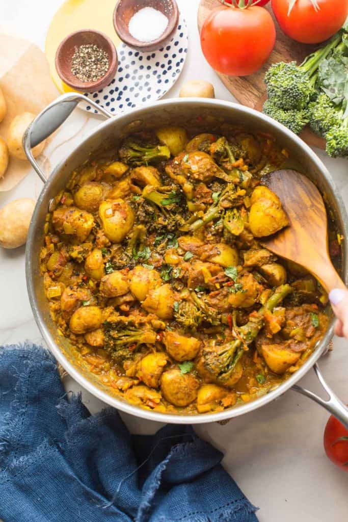 broccoli and potato curry in a large skillet surrounded by the fresh ingredients