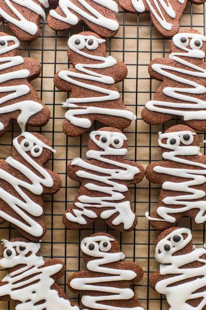 chocolate sugar cookies decorated like mummies on a wire rack