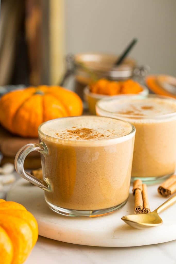 a couple of Dairy Free Pumpkin Spice Lattes topped with cinnamon with little pumpkins and cinnamon sticks