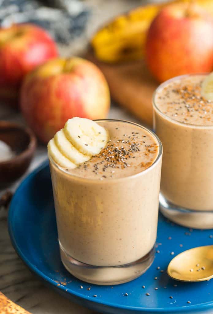 a peanut butter apple banana smoothie in a glass cup with banana slices and chia seeds sprinkled on top