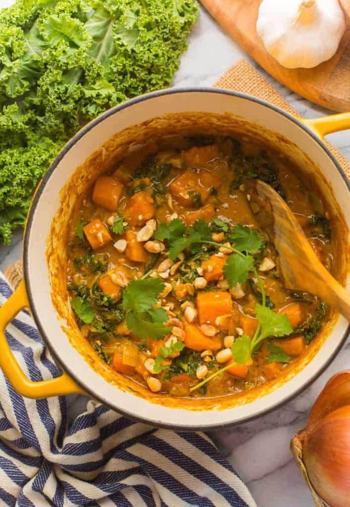Satay Sweet Potato Curry in a big pot with fresh kale, garlic and cilantro