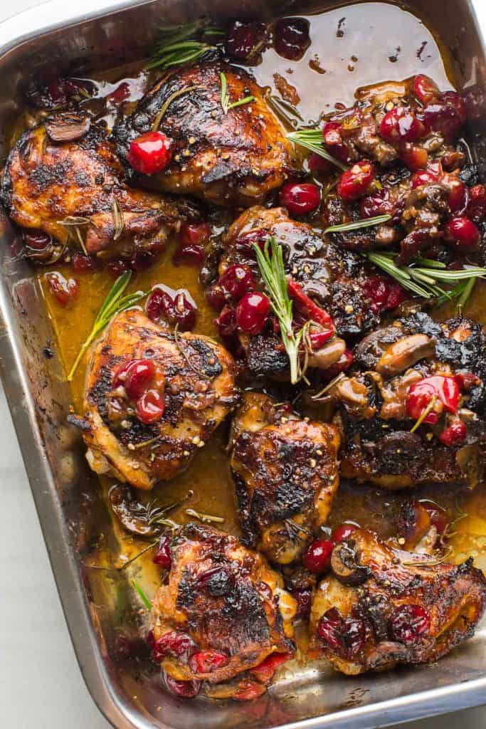 Cranberry Chicken Thighs in a roasting pan topped with rosemary