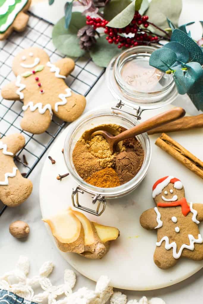 homemade gingerbread spice in a jar surrounded by gingerbread cookies