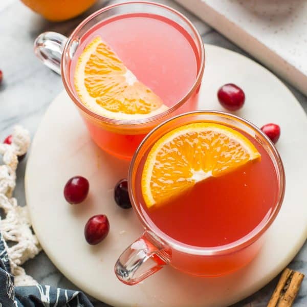 two mugs of instant pot cranberry orange juice with orange slices on top