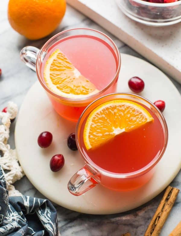 two mugs of instant pot cranberry orange juice with orange slices on top