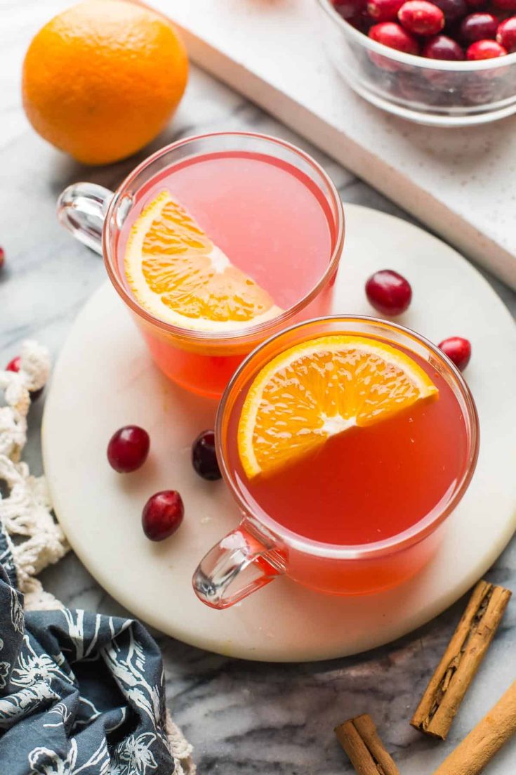 two mugs of instant pot cranberry orange juice with orange slices on top