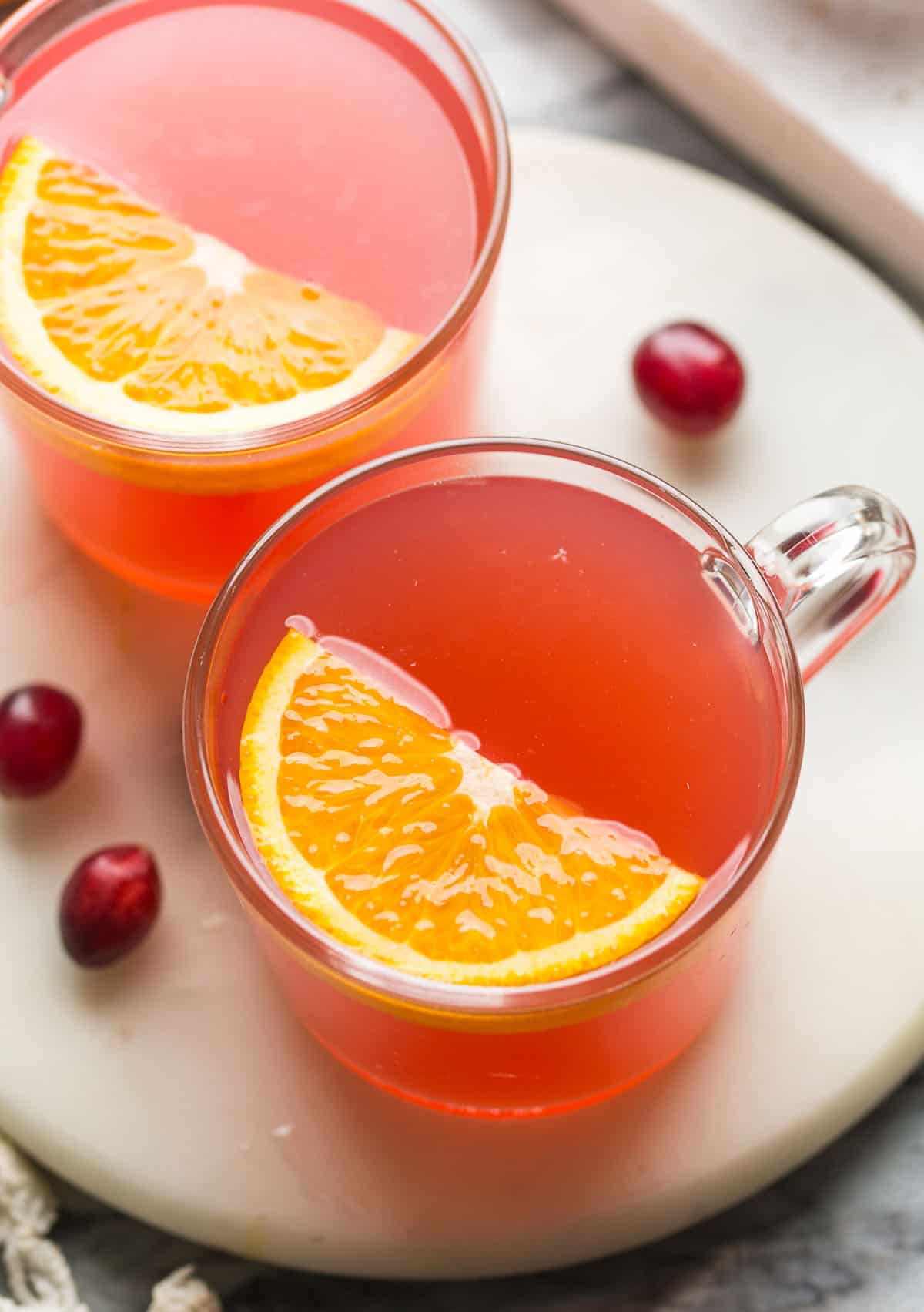 A glass mug containing a pink drink with half an orange slice.