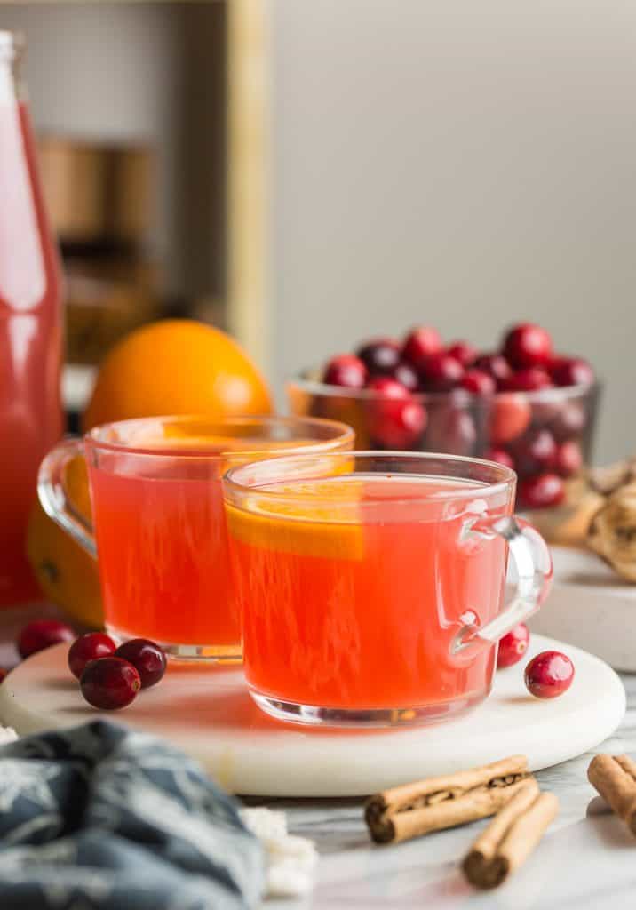 two mugs of instant pot cranberry orange juice with orange slices on top