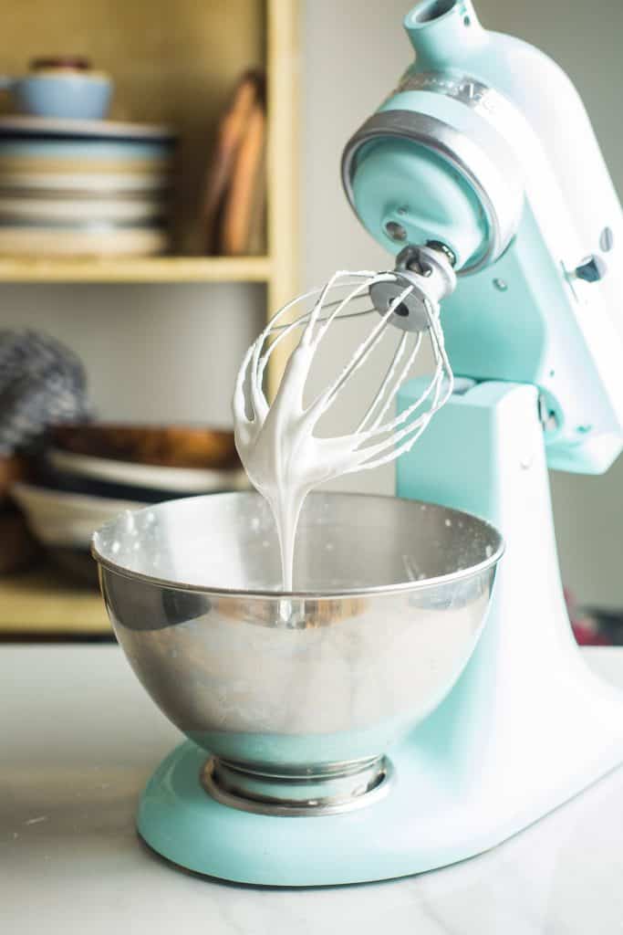 kitchen aid stand mixer opened up with royal icing dripping off the whisk attatchment