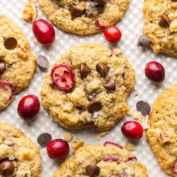 Chocolate-Chip-Cranberry-Oatmeal-Cookies on a baking sheet surrounded by fresh cranberries, walnuts and chocolate chips