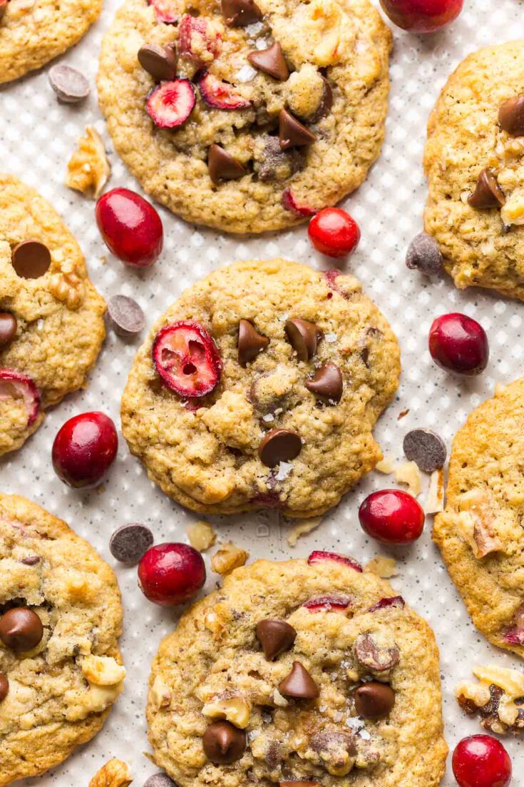 Chocolate-Chip-Cranberry-Oatmeal-Cookies on a baking sheet surrounded by fresh cranberries, walnuts and chocolate chips