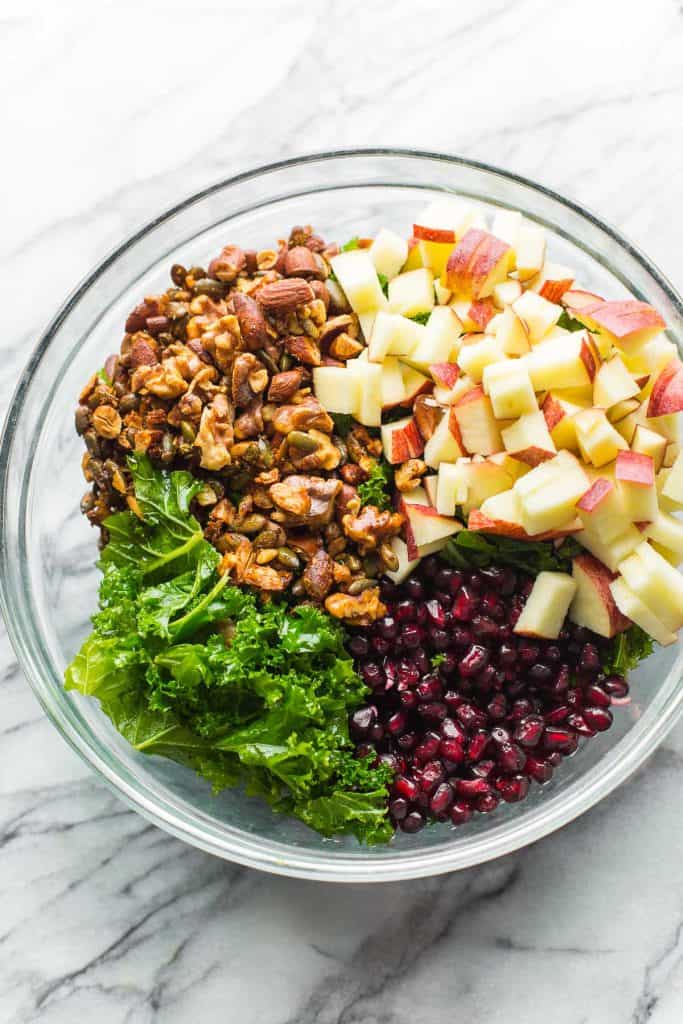 ingredients for a Winter Kale Salad in a big bowl: walnuts, almonds and pumpkin seeds, apples, pomegranate seeds and kale