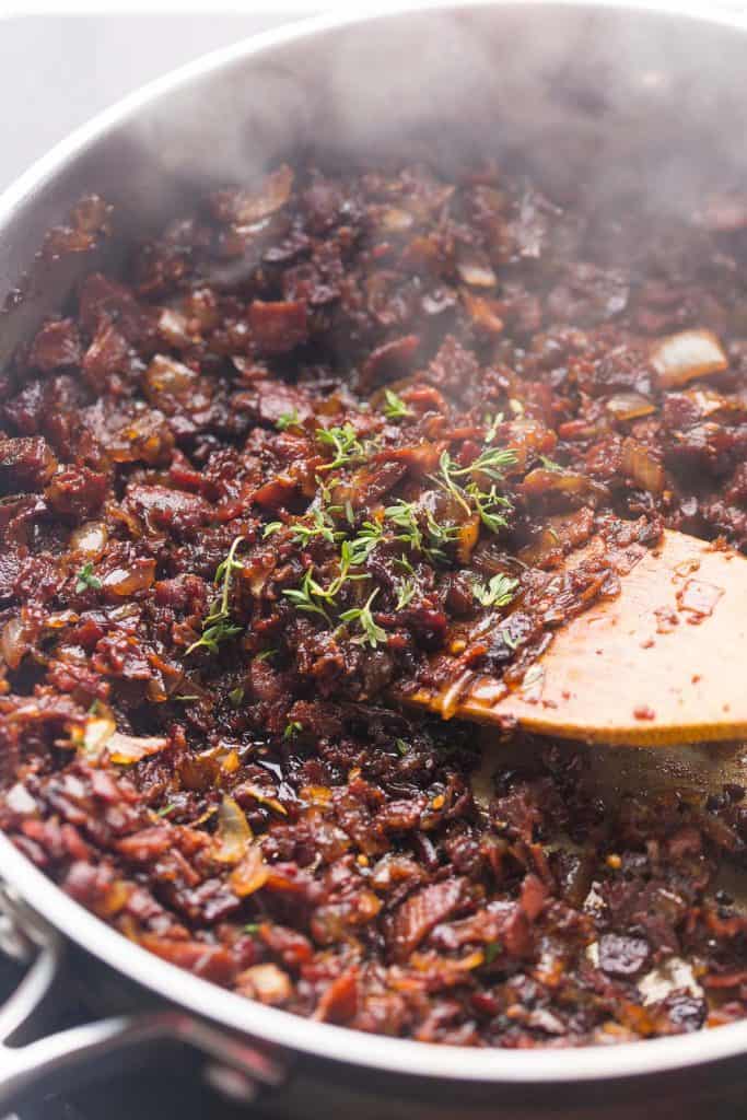 Bacon Jam with Coffee Liqueur in a skillet topped with fresh thyme leaves getting mixed with a wooden spatula