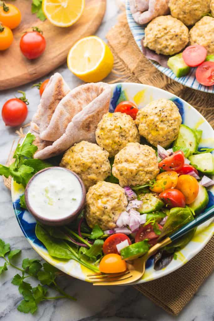 A salad made with tomatoes, cucumber, red onion and topped with greek chicken meatballs 