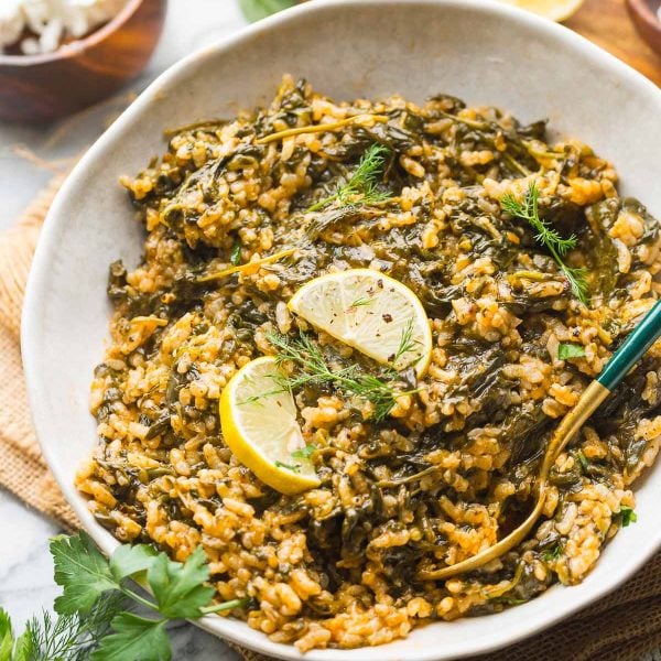 spanakorizo in a serving bowl with lemon wedges and serving utensils