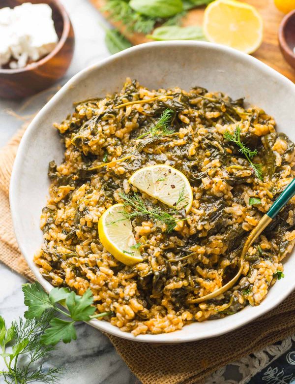 spanakorizo in a serving bowl with lemon wedges and serving utensils