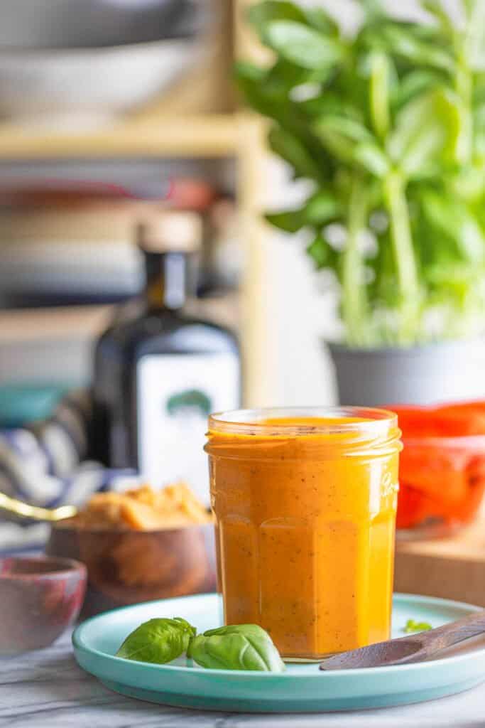 red pepper miso dressing in a storage jar on a plate with fresh ingredients nearby