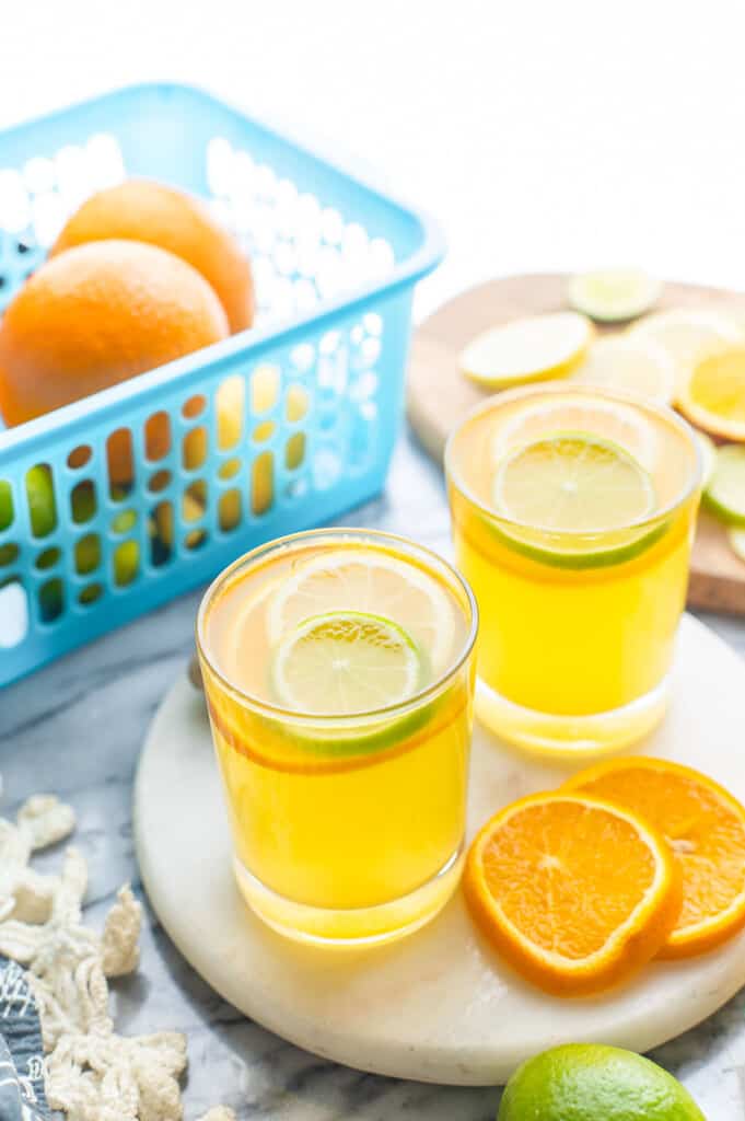 two glasses of a homemade electrolyte drink topped with lemon, orange and lime slices on a platter