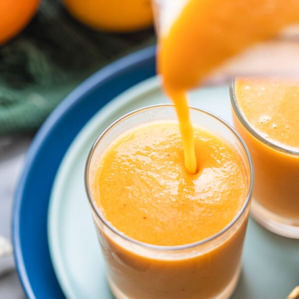 orange creamsicle smoothie pouring into a small glass from blender