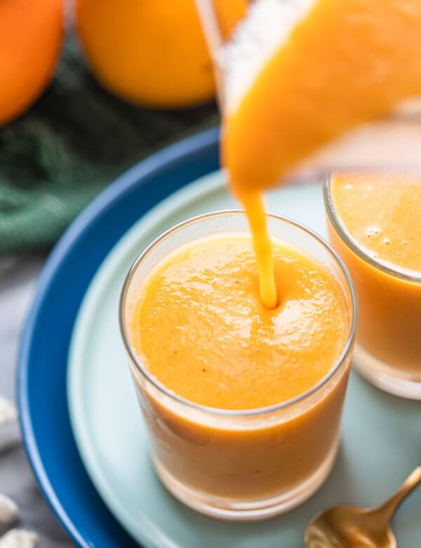 orange creamsicle smoothie pouring into a small glass from blender
